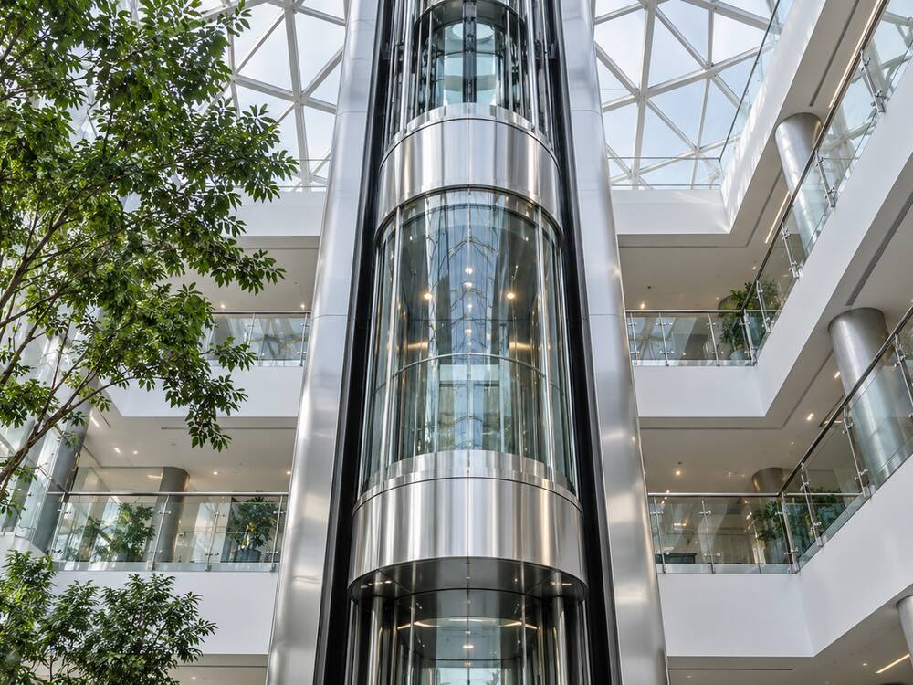 Panoramic glass elevator rising through an office atrium