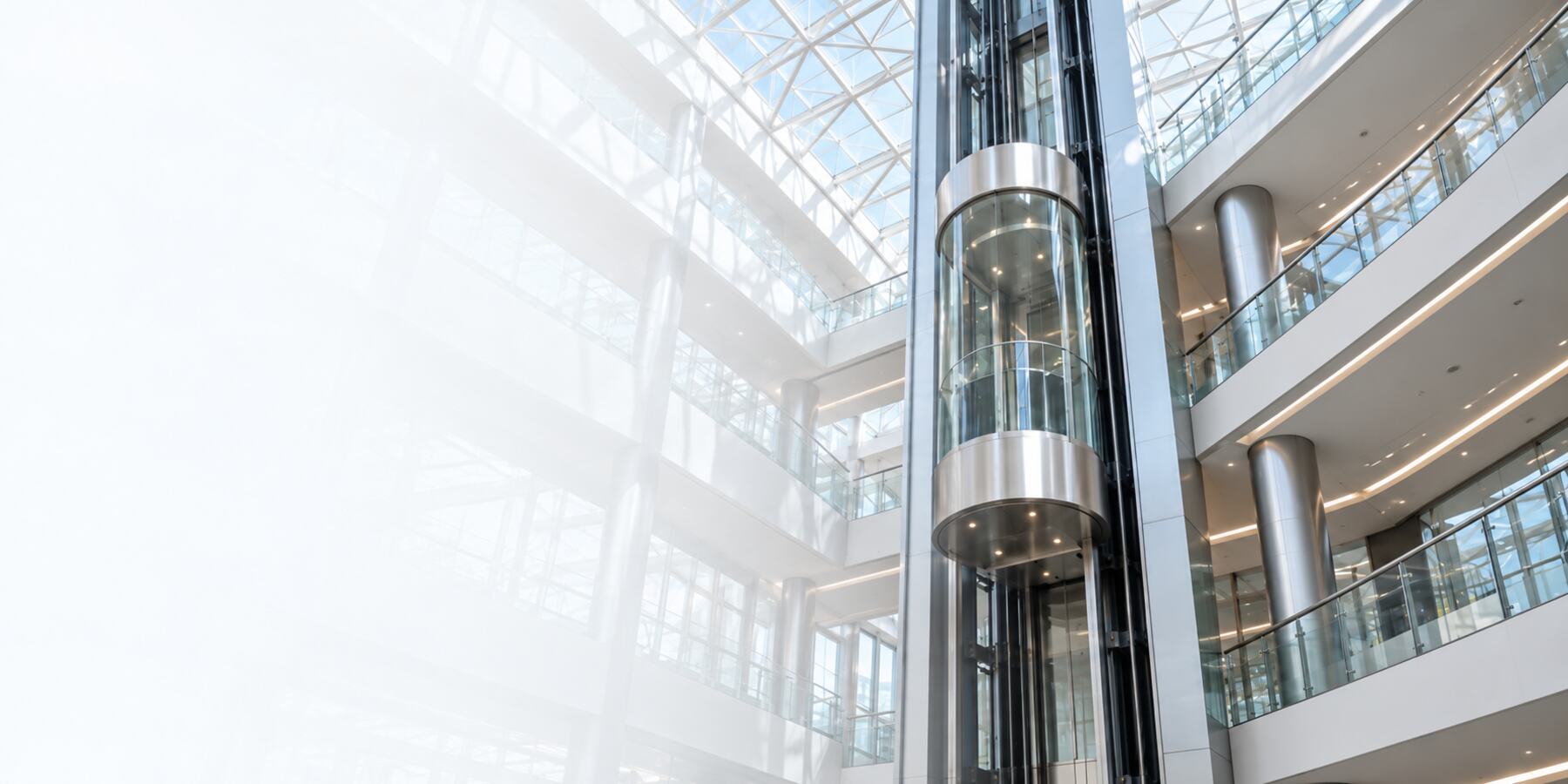 Panoramic glass elevator in a bright office atrium under a glass skylight