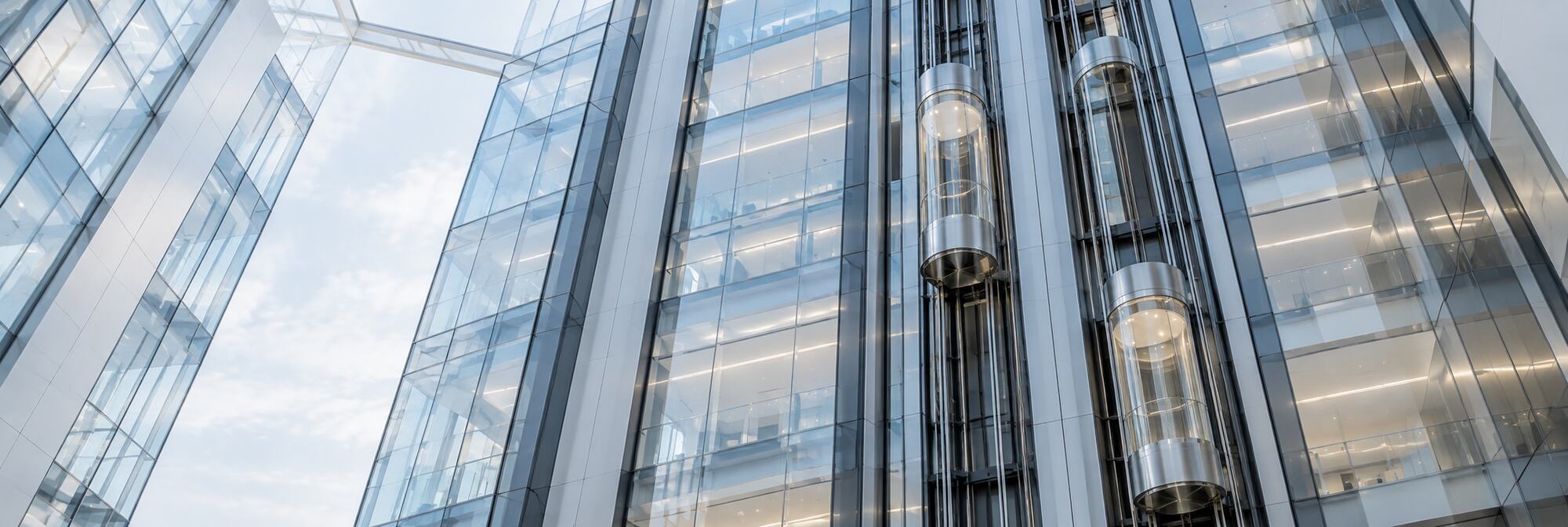 Glass office tower facade with full-height panoramic elevator shafts