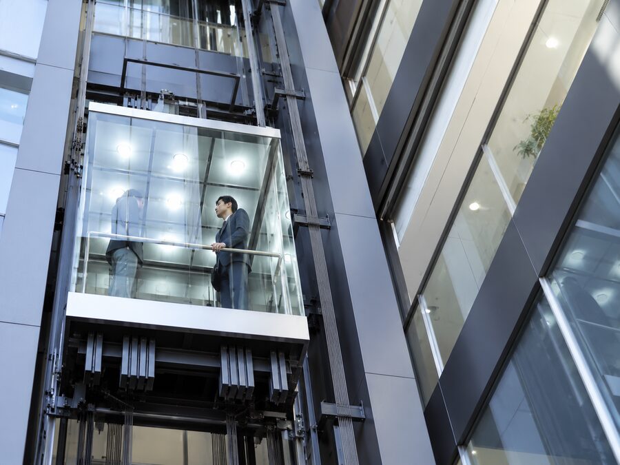 Glass panoramic elevator rising between steel columns, seen from below